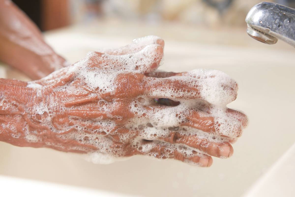 how to clean reusable gloves: close-up of hands rinsing yellow reusable cleaning gloves under running water with mild soap